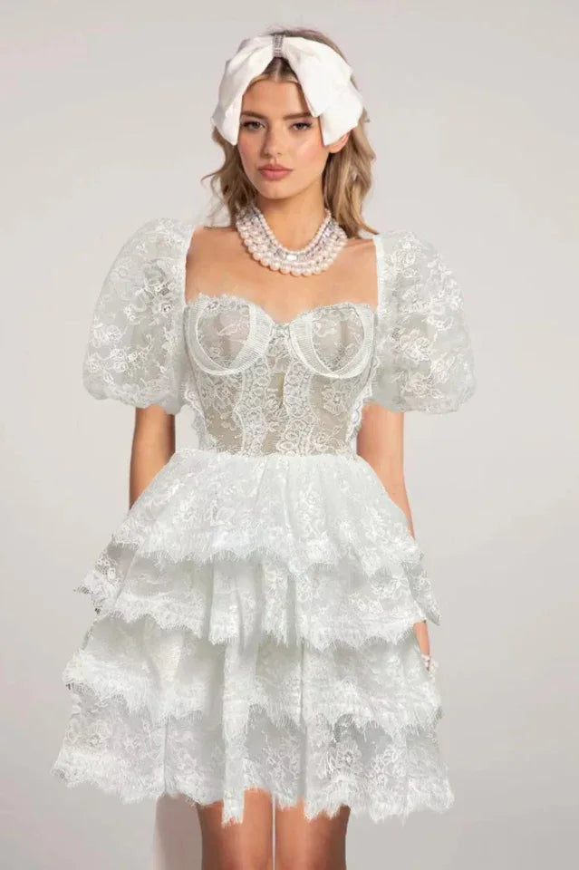 Full body shot of a woman in a white chiffon mini dress with balloon sleeves.