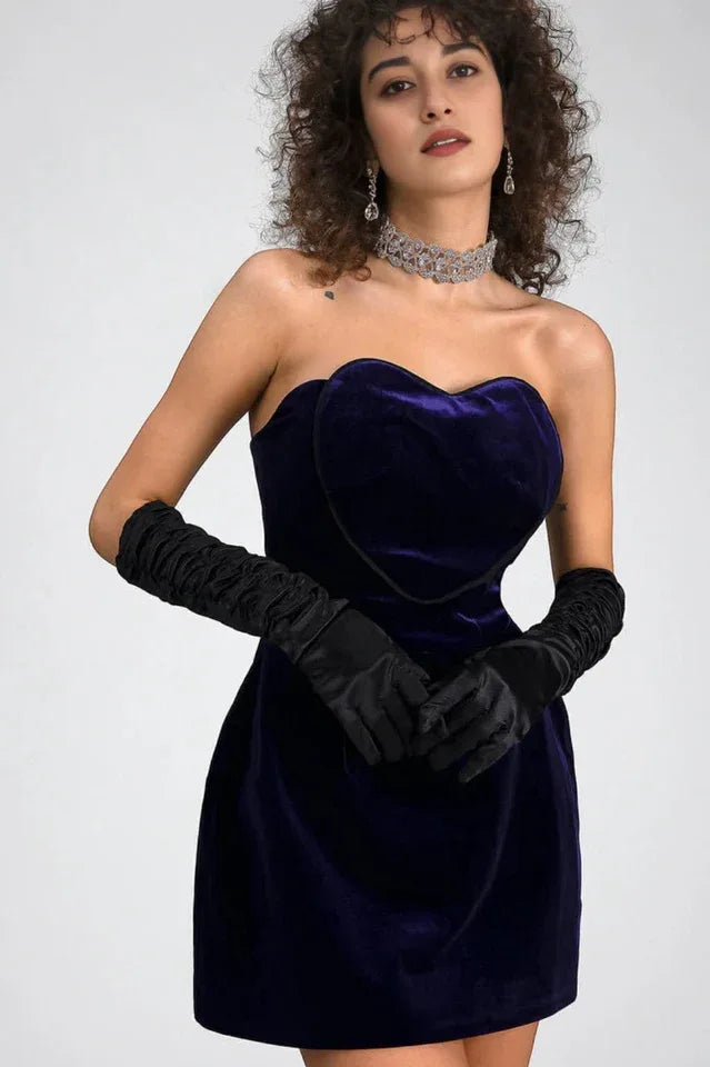 Woman in a purple velvet strapless mini dress with a sweetheart neckline and long black opera gloves, wearing a crystal choker and statement earrings. Main image