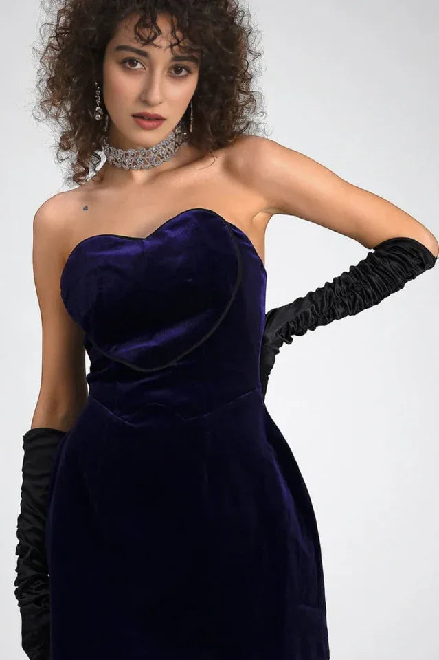 Close-up of a woman in a purple velvet strapless mini dress with a sweetheart neckline and long black opera gloves.
