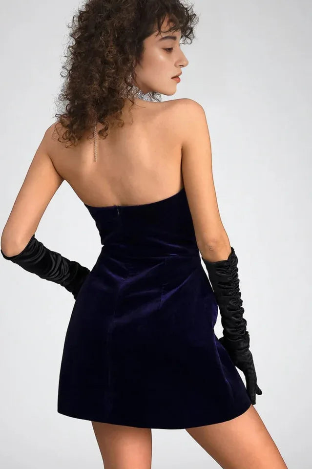 Back view of a woman in a purple velvet strapless mini dress with a sweetheart neckline and long black opera gloves.