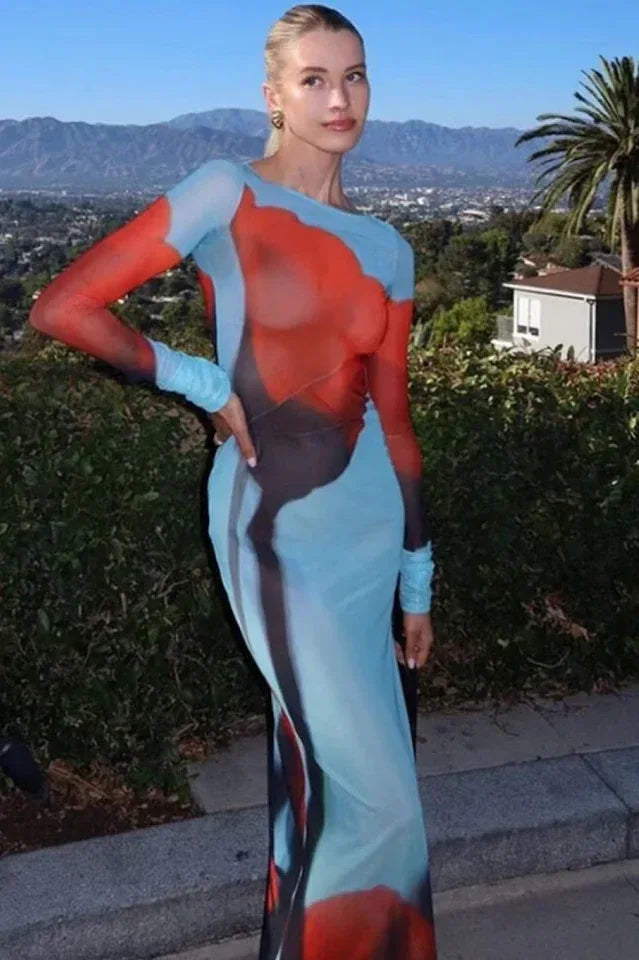 Woman posing outdoors in a long, sheer, light blue dress with an abstract red and black floral print, long sleeves, and a high slit.