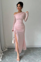 Full-length view of a woman in a pink one-shoulder ruched maxi dress holding a white handbag.