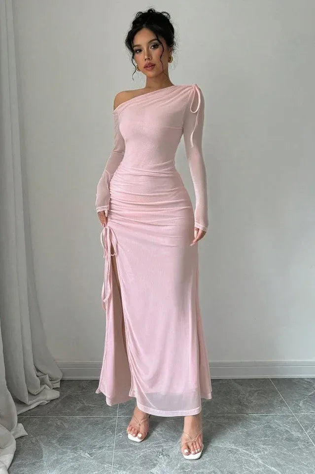 Woman wearing a light pink one-shoulder ruched maxi dress with a drawstring side slit and long sleeves.