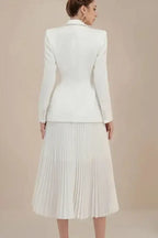 Rear view of a woman in a white pleated midi skirt suit, showcasing the back of the blazer.