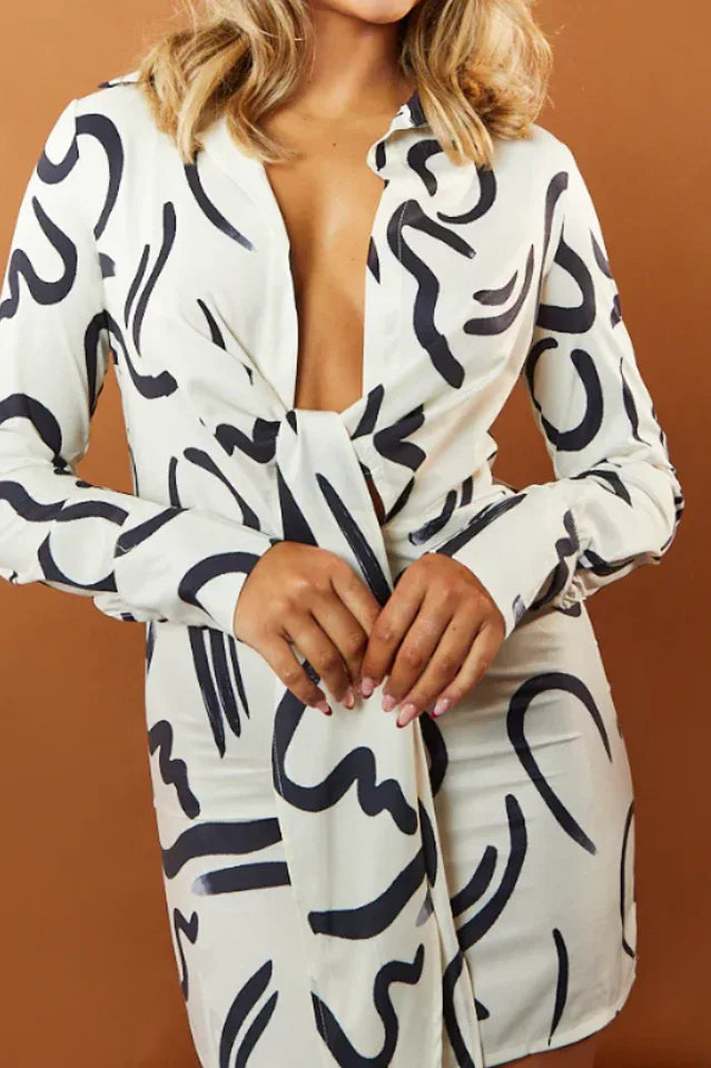 Close-up of a woman in a white and black abstract print satin mini dress with a tie front.
