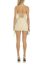 Back view of a woman in a strapless sequined mini dress with ruched detailing, a draped overlay, and corset back