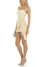 Side view of a woman wearing a strapless sequined mini dress with ruched detailing and a draped overlay
