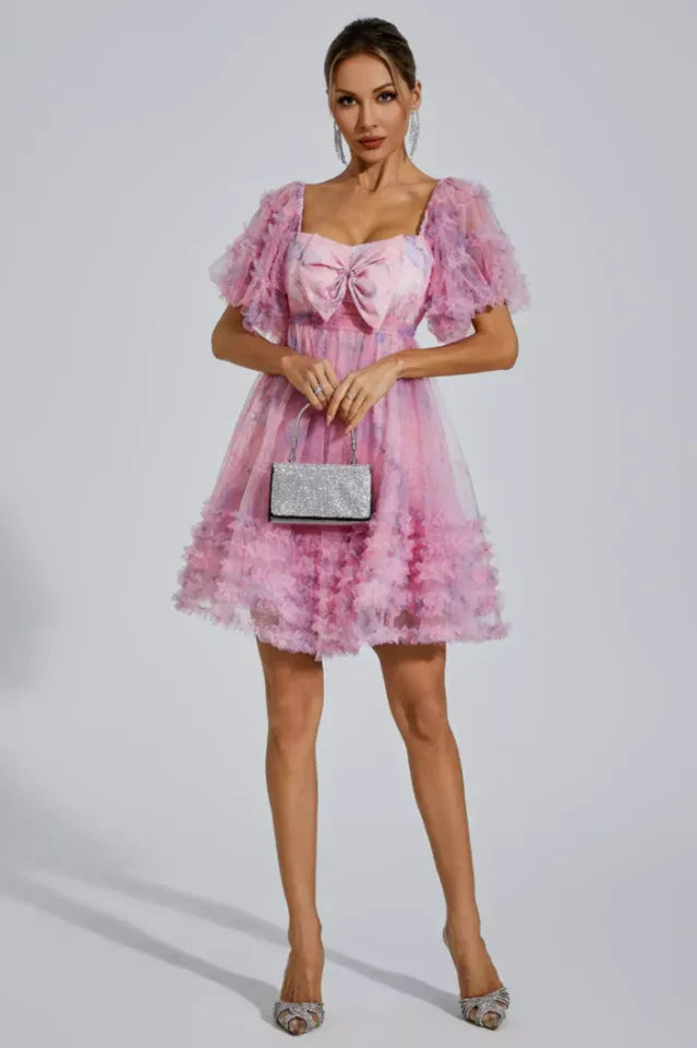 Woman holding a silver clutch and wearing a pink floral print tulle dress with ruffled sleeves and hem
