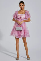 Woman holding a silver clutch and wearing a pink floral print tulle dress with ruffled sleeves and hem