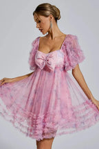 Woman wearing a pink floral print tulle dress with a large bow on the bust and ruffled sleeves