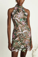 Woman wearing a sleeveless, sheer mini dress with colorful floral embroidery and sequins, featuring a halter neckline.