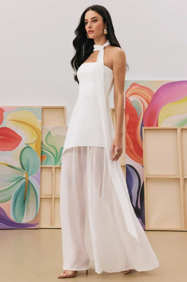 Woman in a white halter neck maxi dress with a high slit and sheer overlay, viewed from the side.