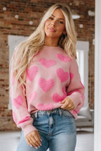 Woman wearing a pink knit sweater with a textured all-over heart pattern and crew neckline.