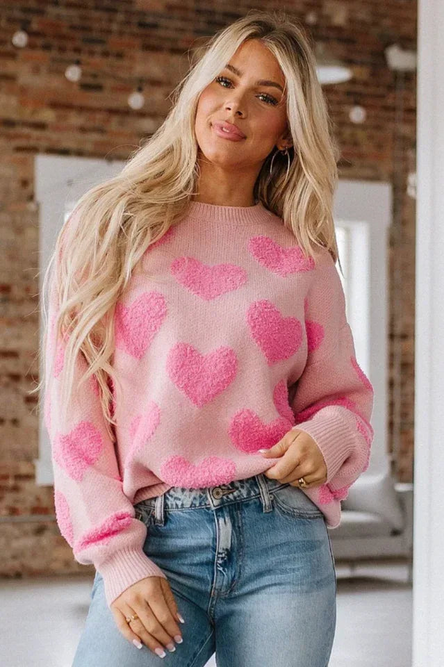 Woman wearing a pink knit sweater with a textured all-over heart pattern and crew neckline.