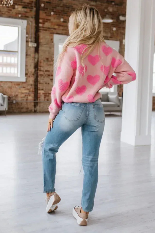 Back view of a woman in a pink sweater with heart pattern and distressed denim.