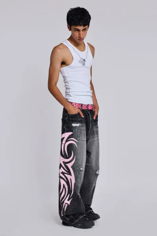 Man wearing a white tank top and baggy black jeans with pink tribal print, with hands in pockets