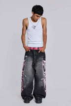 Man wearing a white tank top and baggy black jeans with pink tribal print