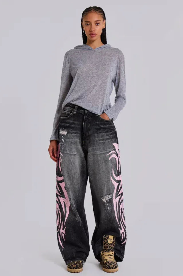 Woman wearing a grey hooded top and baggy black jeans with pink tribal print Main image