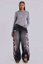 Woman wearing a grey hooded top and baggy black jeans with pink tribal print