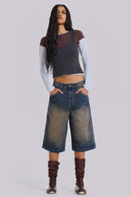 Woman wearing dark wash wide leg cropped denim culottes with a dark grey tank top layered over a light blue long-sleeve shirt and brown boots.