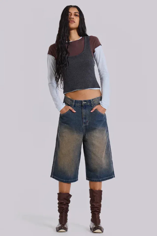 Woman wearing dark wash wide leg cropped denim culottes with a dark grey tank top layered over a light blue long-sleeve shirt and brown boots.