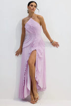 Woman wearing a lavender pleated maxi dress with a high slit and halter neckline, posing against a white background.