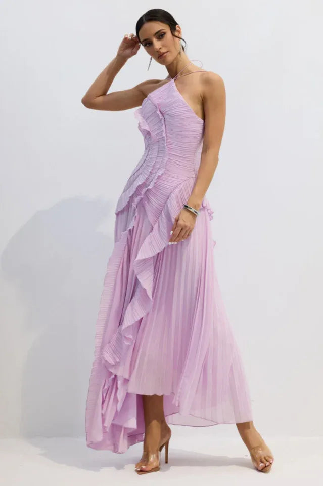 Model in a lavender pleated formal dress with a high slit and halter strap, standing with one hand on her head.