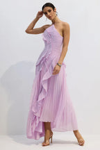 Model in a lavender pleated formal dress with a high slit and halter strap, standing with one hand on her head.