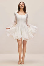 Woman in a white mini dress with a sweetheart neckline and dramatic ruffled skirt.