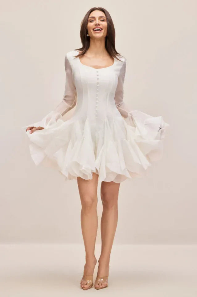 Woman in a white mini dress with a sweetheart neckline and dramatic ruffled skirt.