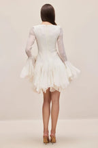 Back view of a white dress with long sheer sleeves and a flounced hem.