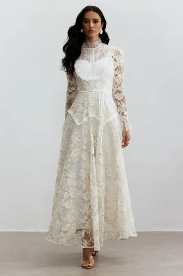 Woman wearing a long white lace gown with a high ruffled neckline and long sleeves.