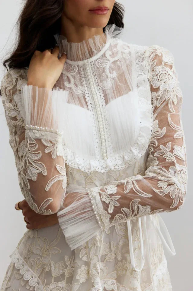 Close-up of the intricate lace detailing, pearl embellishments, and ruffled neckline of a white gown.