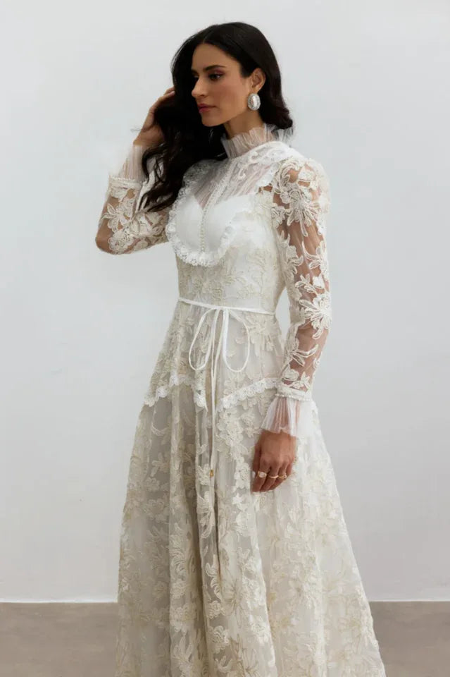 Side profile of a woman modeling a white long-sleeved lace formal dress with a high neck.
