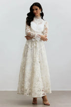 Full-length view of a woman in a white lace formal gown with her arms crossed.