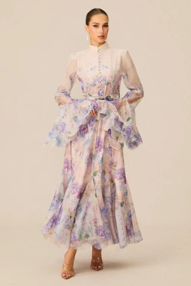 Full-length view of a woman in a pastel floral print maxi dress with dramatic bell sleeves and a self-tie waist.