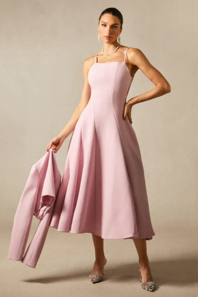 Woman holding a pink jacket while wearing a pink formal dress with thin straps and a flared skirt.