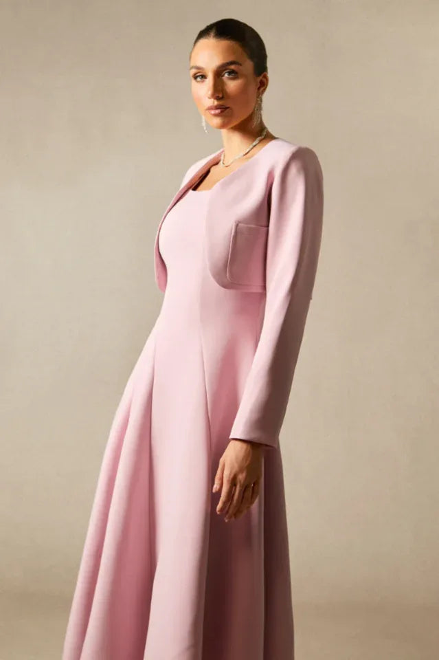 Side profile of a woman in a pink formal dress and jacket, emphasizing the fabric texture and silhouette.