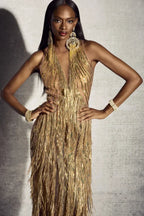 Woman wearing a gold sequined and fringed halter gown, posing with hands on hips.