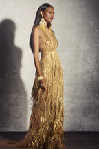 Woman wearing a gold sequined and fringed halter gown, side view.