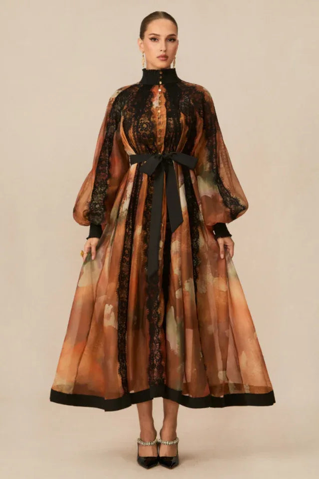 Woman wearing a long, flowing A-line dress with a high neckline, puffed sleeves, and a black ribbon belt. Main image