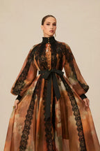 Woman posing in a floor-length sheer printed dress with a black lace overlay on the bodice and sleeves.