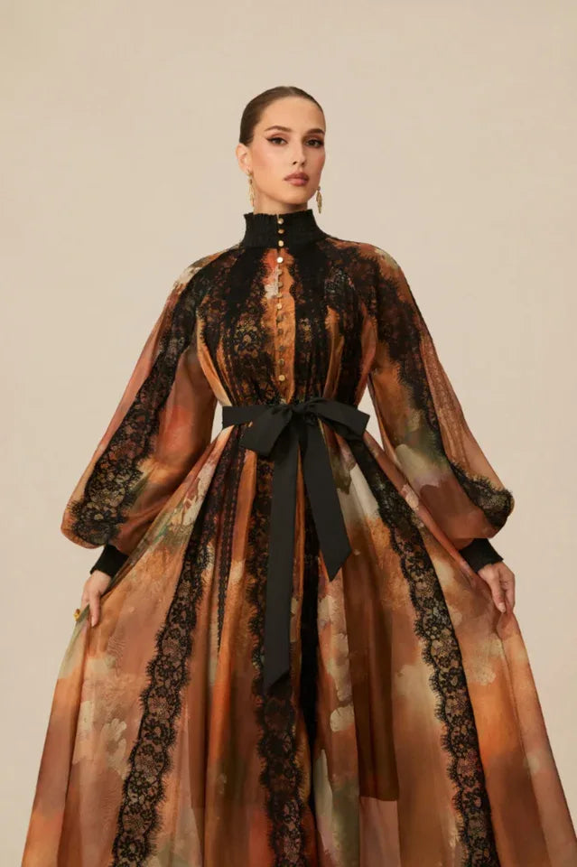 Woman posing in a floor-length sheer printed dress with a black lace overlay on the bodice and sleeves.
