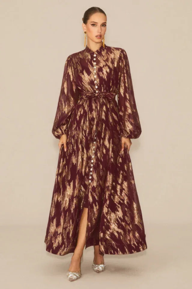 Woman wearing a burgundy and gold abstract print maxi dress with a high neck and balloon sleeves