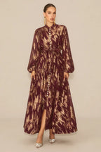 Woman wearing a burgundy and gold abstract print maxi dress with a high neck and balloon sleeves