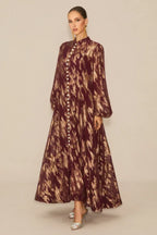 Woman posing in a burgundy and gold abstract print maxi dress with a slit