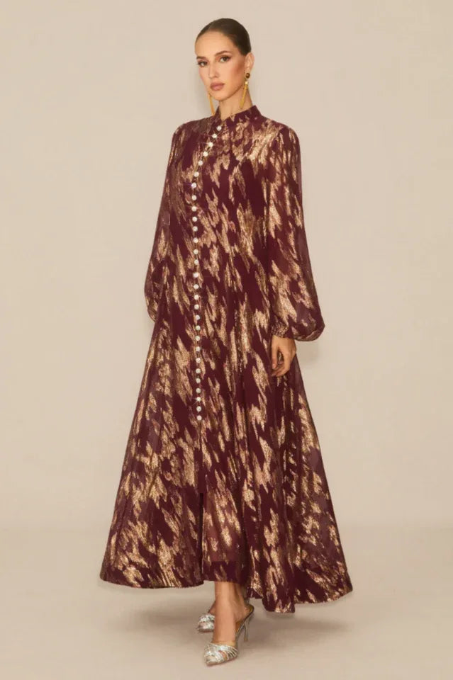 Woman posing in a burgundy and gold abstract print maxi dress with a slit