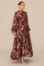 Model showcasing a burgundy and gold abstract print maxi dress with a self-tie belt