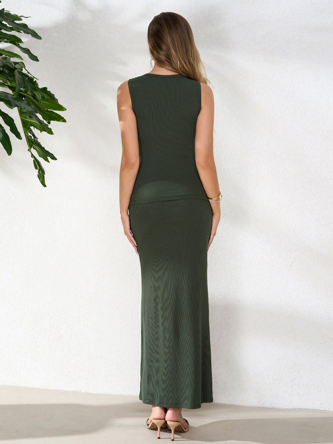 Woman wearing a dark green ribbed knit sleeveless collared button-up top and a matching high-waisted column maxi skirt, holding a straw handbag.