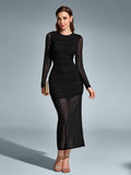 Woman holding a gold clutch while wearing a black ruched mesh maxi dress